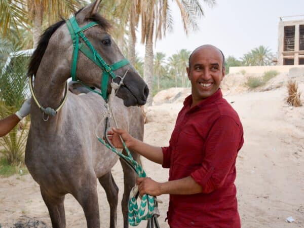 Man in a red shirt smiling while holding a grey horse