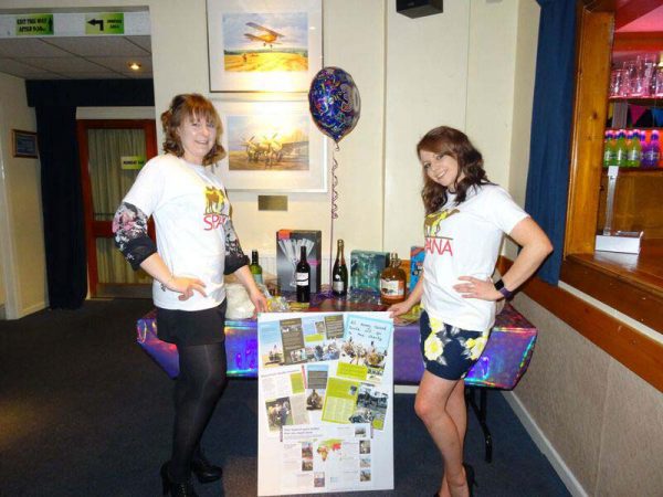 Two women in SPANA tshirts standing next to table