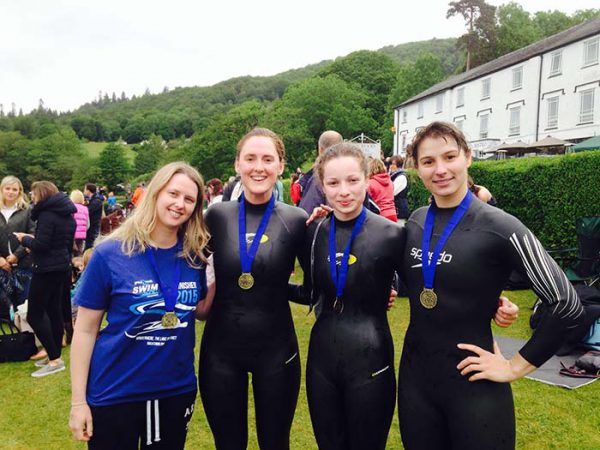 Four smiling women wearing wetsuits and medals